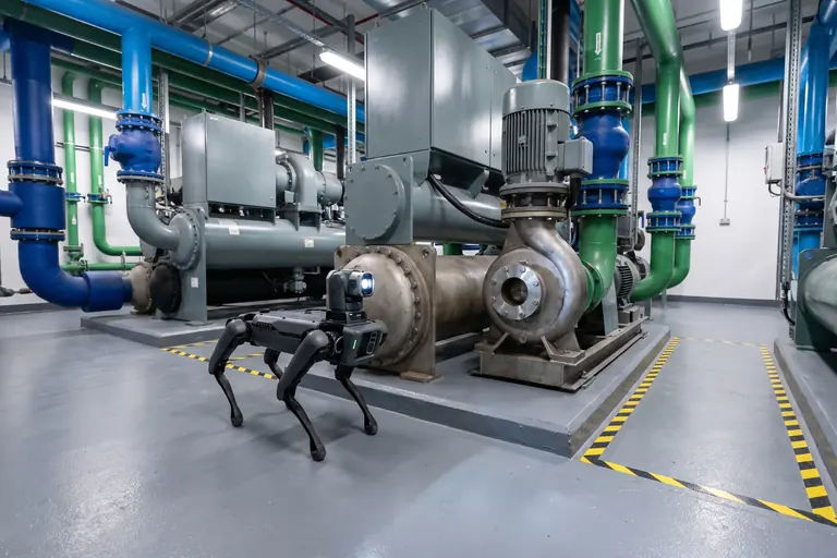 A four-legged inspection robot beside a pump in a data centre plant room with chillers and blue and green pipework.